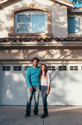 A joyful couple stands in front of their newly purchased home, symbolizing togetherness and success.
